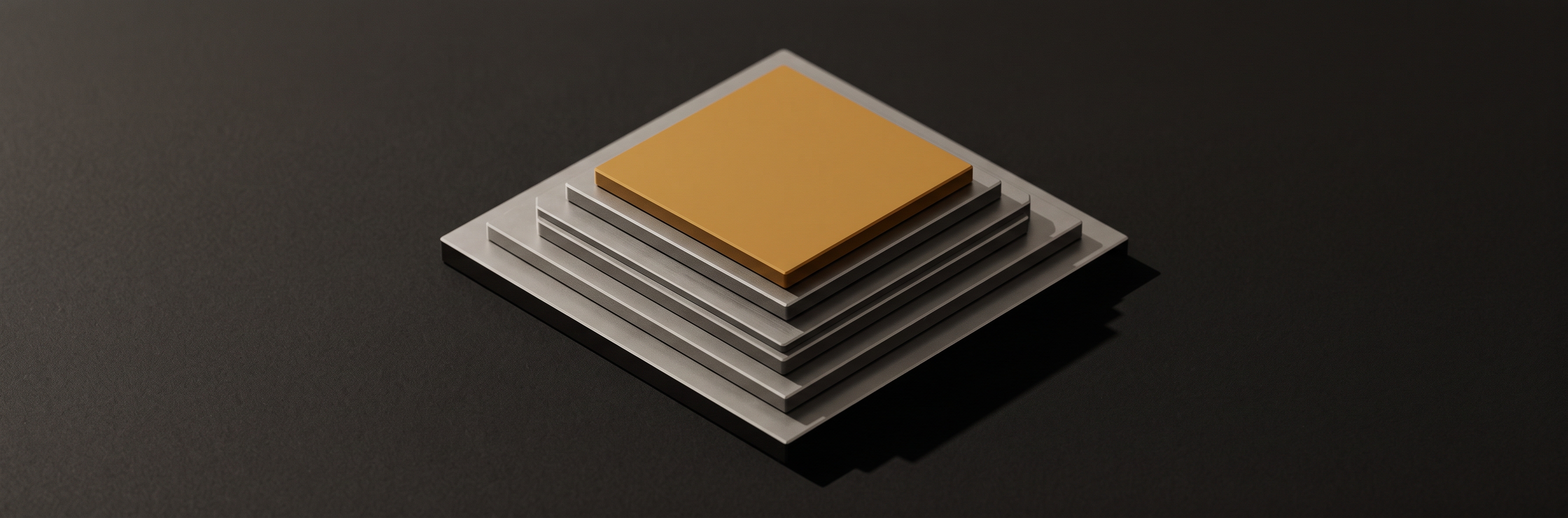 Five flat metal plates of decreasing size stacked directly on top of one another on a dark surface.